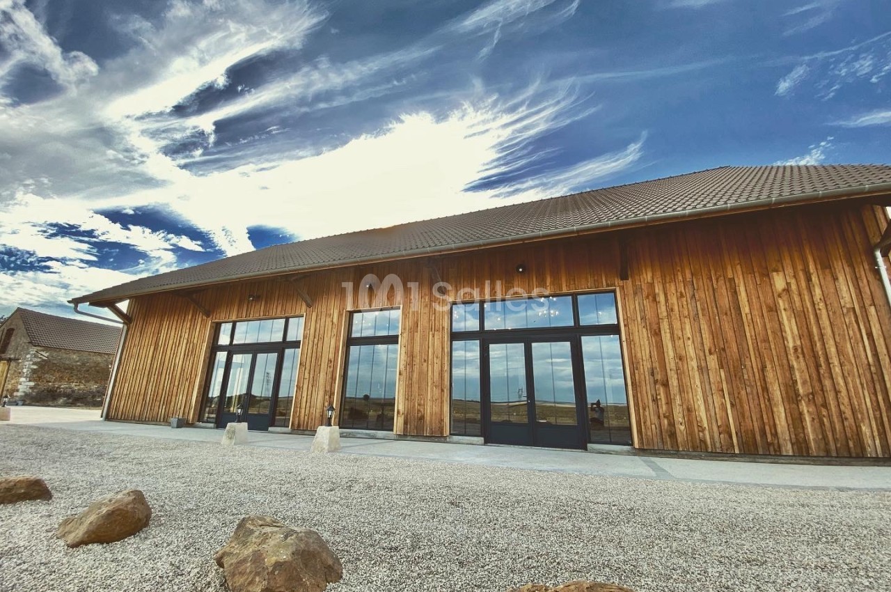 Bâtiment contemporain en bois avec baies vitrées, cour de gravier et ciel dégagé.