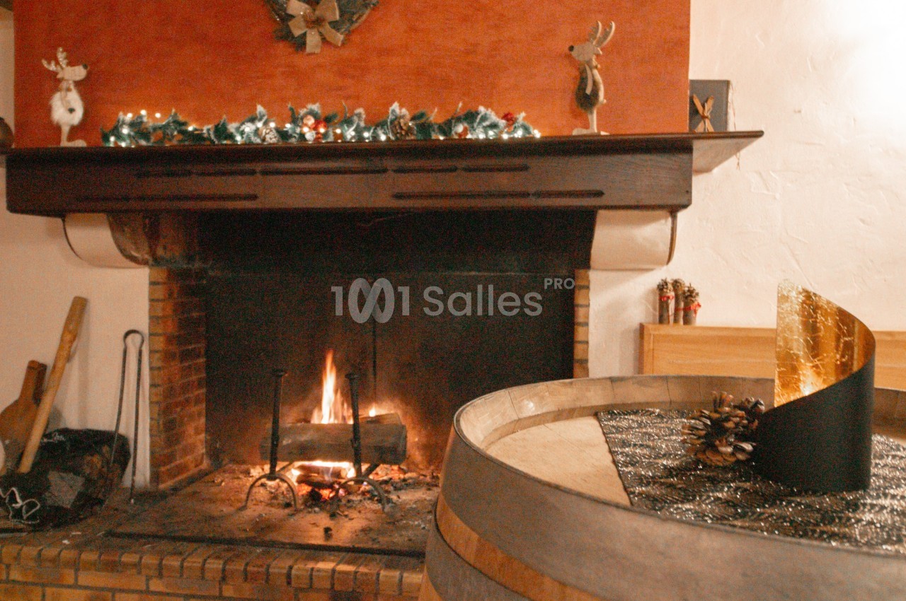 Cheminée en pierre et briques avec un feu de bois allumé, surmontée d'un manteau sombre décoré de guirlandes de Noël, à côté d'un tonneau en bois doré sur le dessus. Let me check length: roughly 165 characters, too long. Need ≤125. Cheminée en briques au
