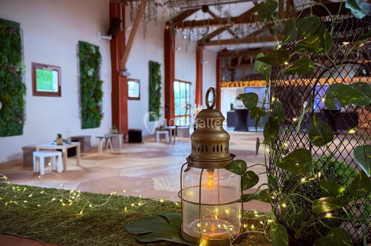 Salle décorée avec des plantes, guirlandes lumineuses et une lanterne en premier plan sur un comptoir végétalisé.