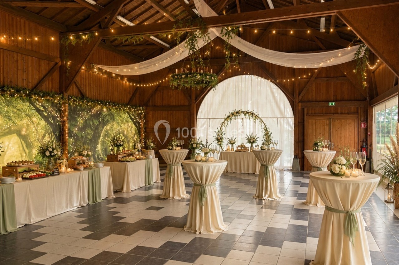 Salle de réception décorée avec des tables hautes, guirlandes lumineuses et drapés blancs dans un cadre boisé.