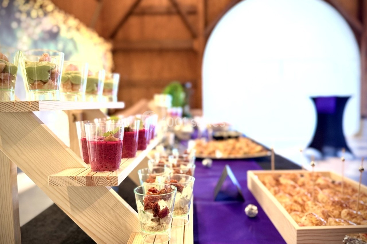 Buffet avec verrines colorées et pâtisseries disposées sur des présentoirs en bois dans une salle lumineuse.