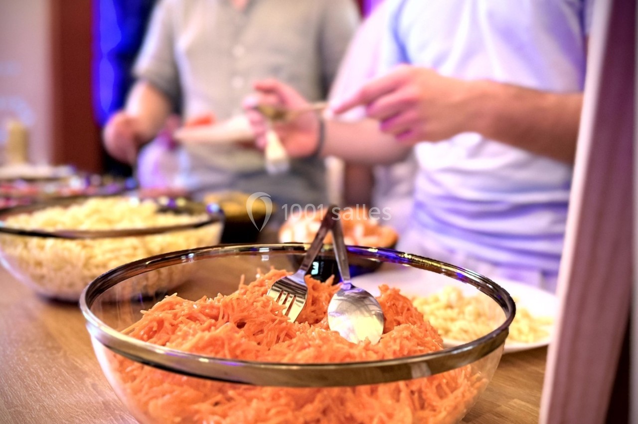 Des personnes se servent dans un buffet comprenant des salades variées, dont des carottes râpées au premier plan.