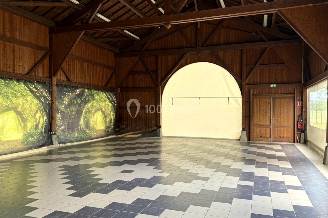 Salle vide avec charpente en bois, murs décorés de fresques forestières et sol carrelé à motifs géométriques.