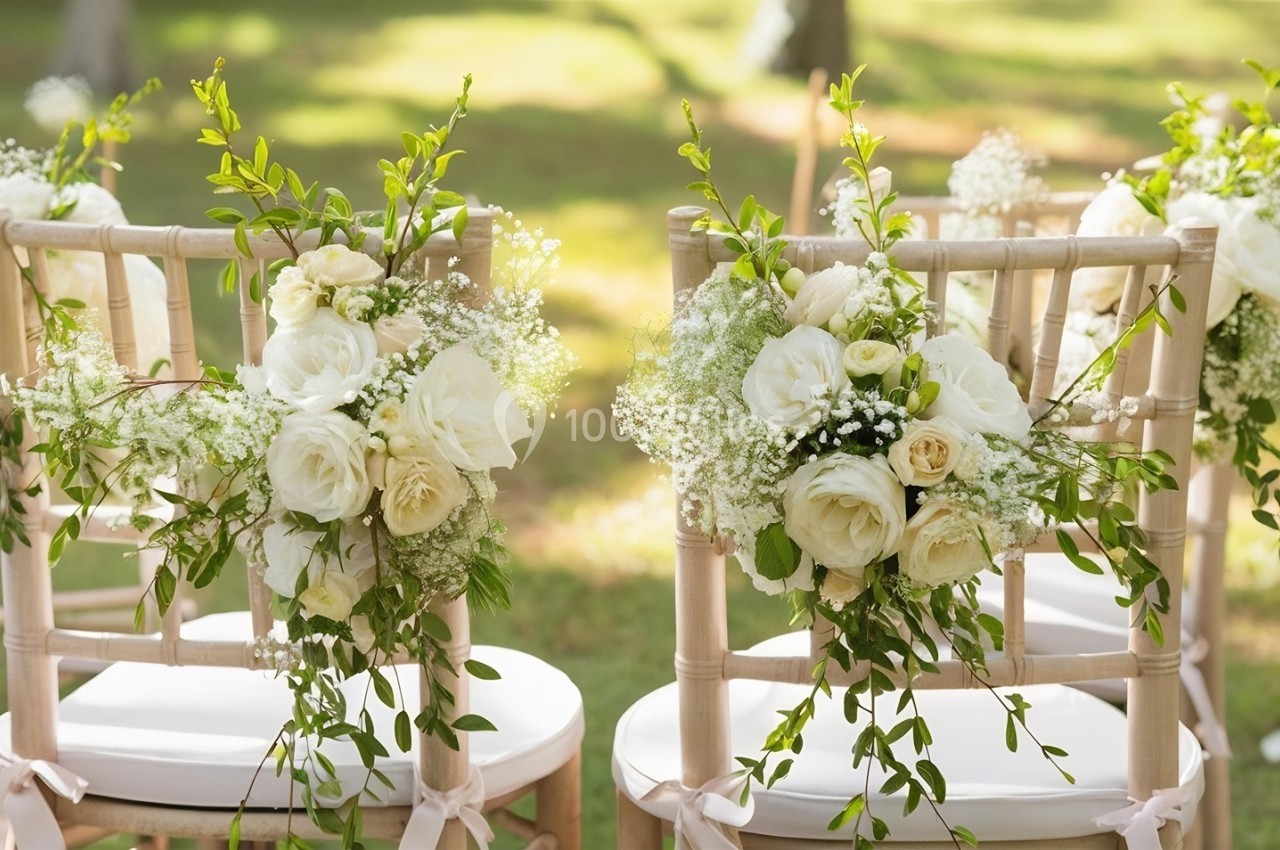Chaises en bois décorées de fleurs blanches et de feuillage, disposées dans un cadre extérieur verdoyant.