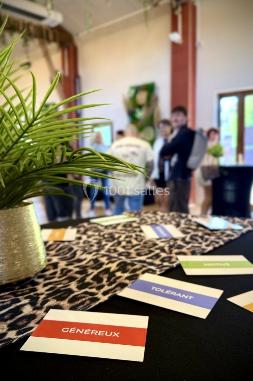 Cartes avec des adjectifs sur une table à motif léopard, dans une salle avec des plantes et des personnes en arrière-plan.