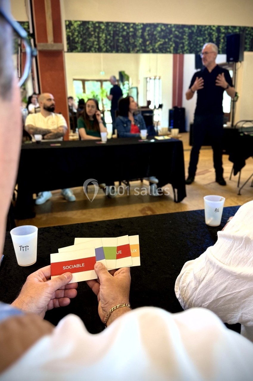 Une personne tient des cartes colorées pendant une présentation interactive dans une salle avec un groupe de participants.