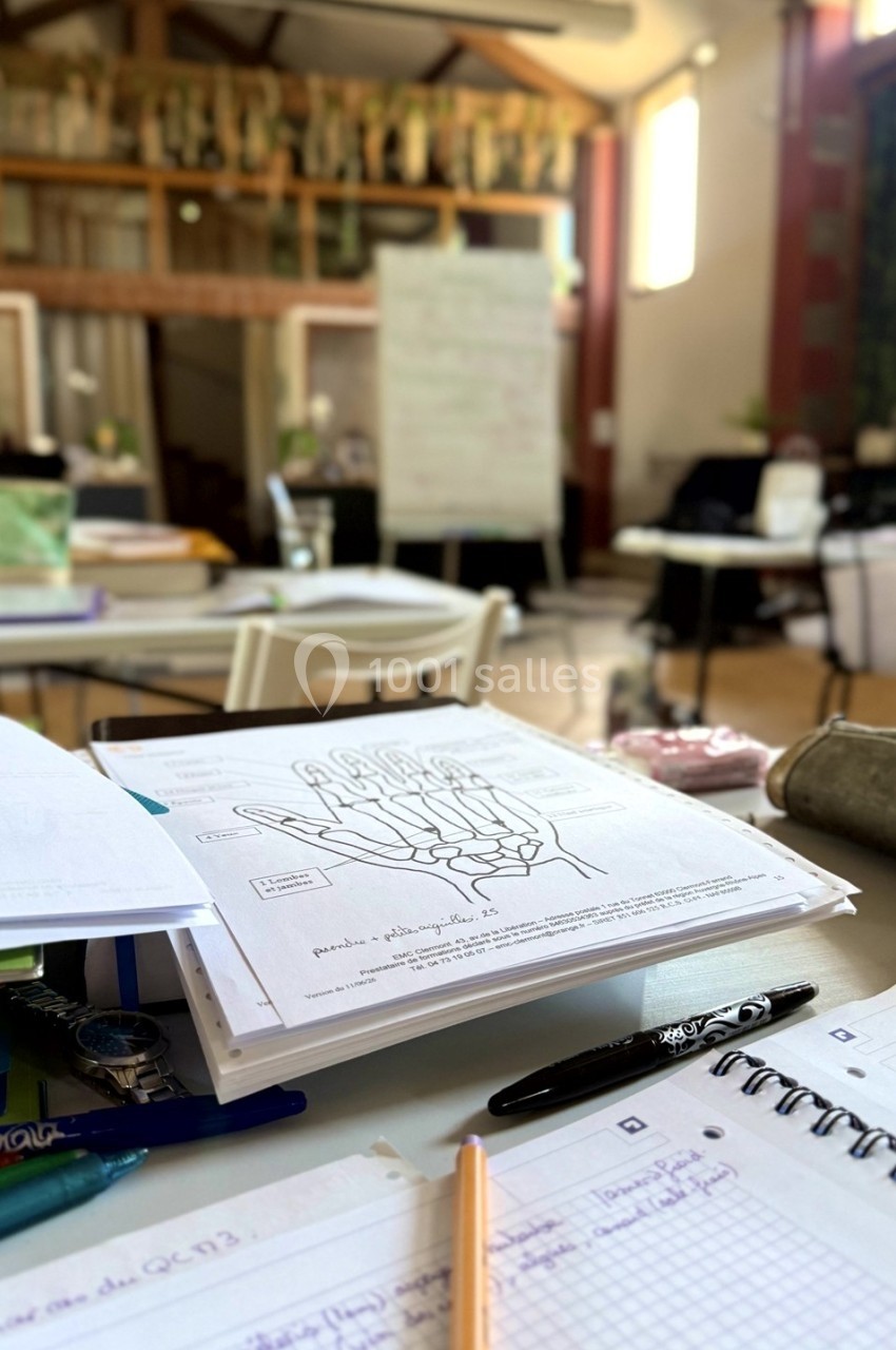 Des documents et cahiers ouverts sur une table dans une salle de classe lumineuse avec un tableau en arrière-plan.