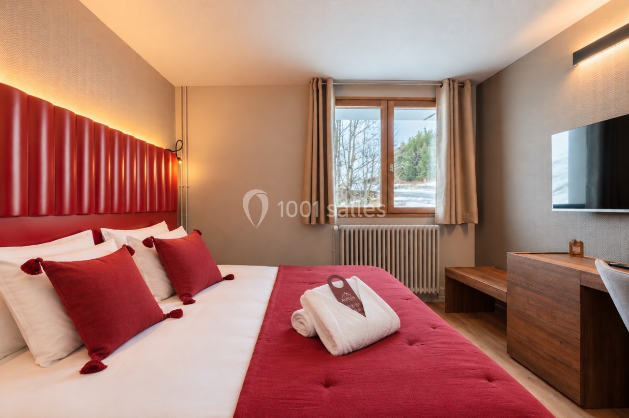 Chambre d'hôtel avec lit double, tête de lit rouge, fenêtre donnant sur un paysage enneigé et mobilier en bois.