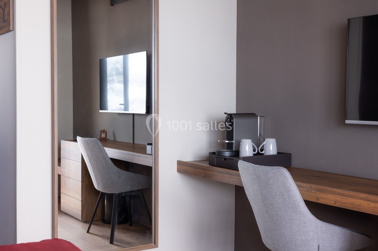Bureau moderne avec chaise grise, machine à café et télévision murale reflétée dans un grand miroir.