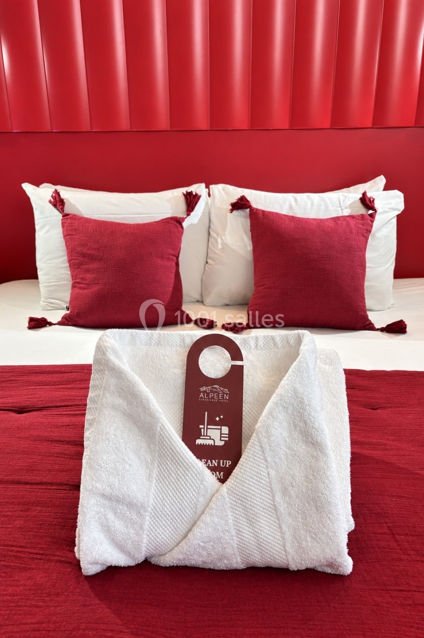 Peignoir blanc plié sur un lit avec draps et coussins rouges, dans une chambre à la décoration assortie.
