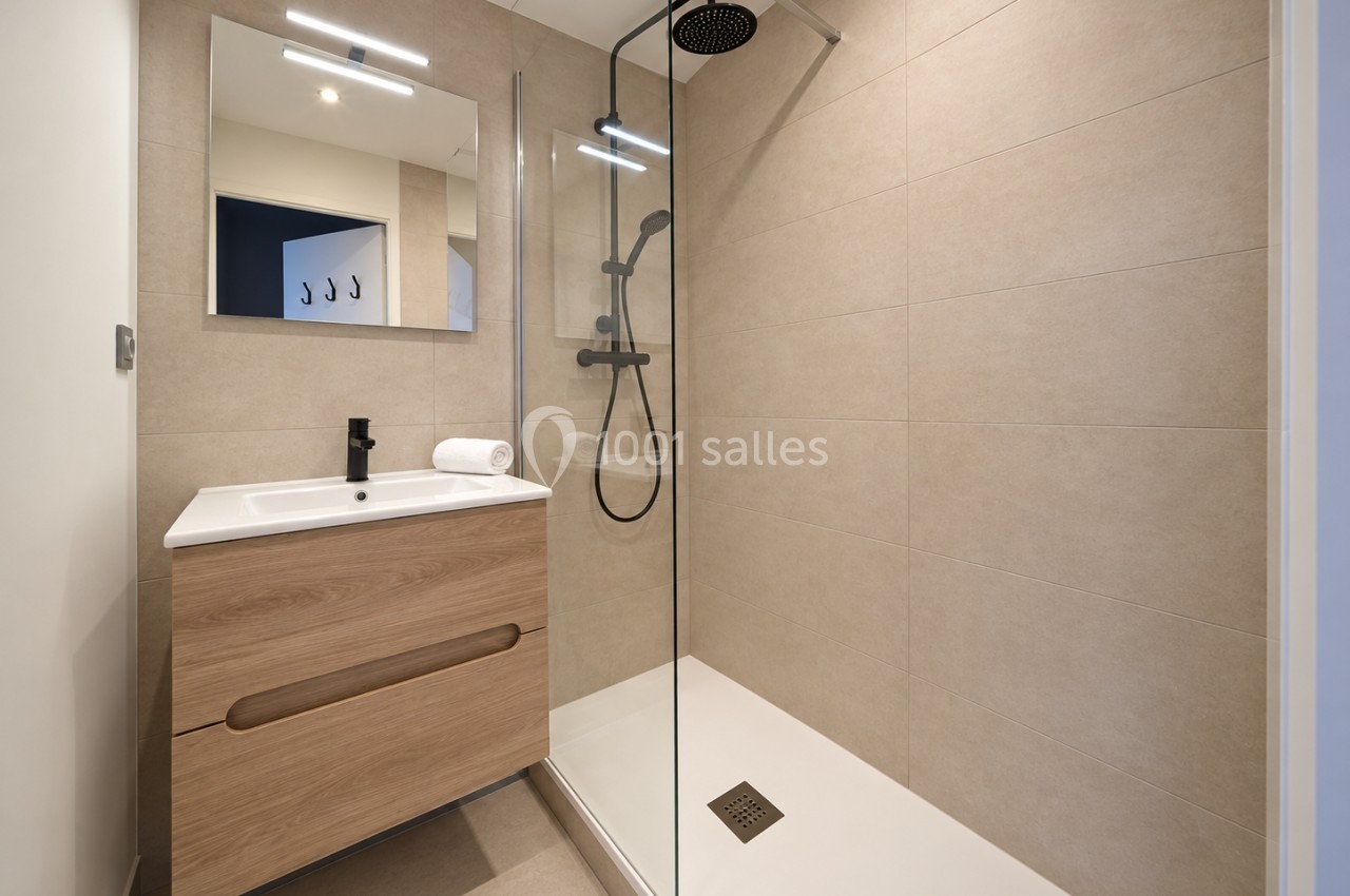 Salle de bain moderne avec douche à l'italienne, meuble en bois clair, miroir et carrelage beige.