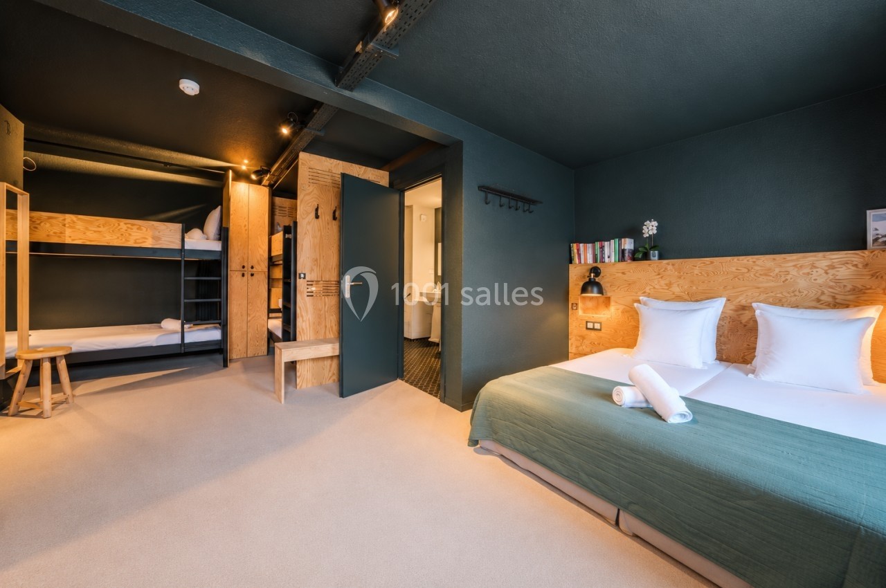 Chambre moderne avec lits superposés, lit double, éclairage chaleureux et salle de bain attenante.