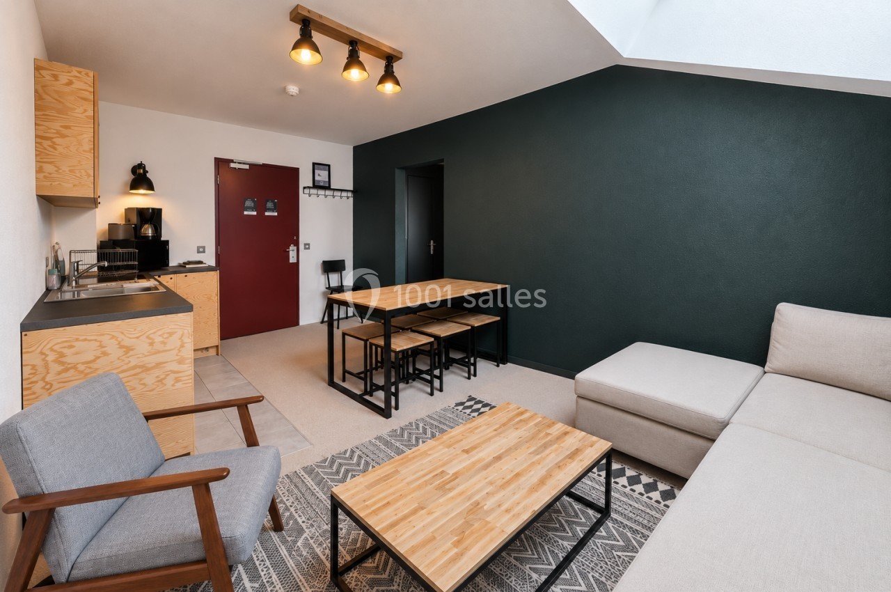 Salon moderne avec canapé beige, table basse en bois, cuisine ouverte et table à manger dans un espace lumineux.