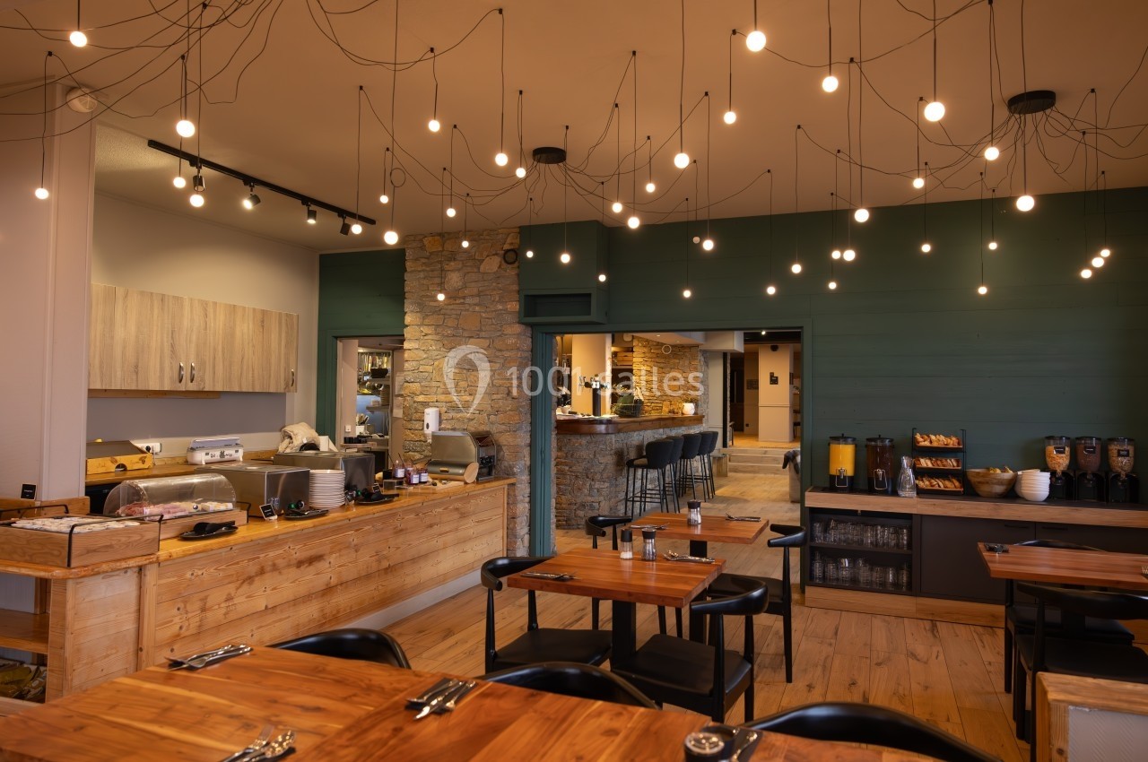 Salle de restaurant moderne avec tables en bois, éclairage suspendu et buffet en arrière-plan.