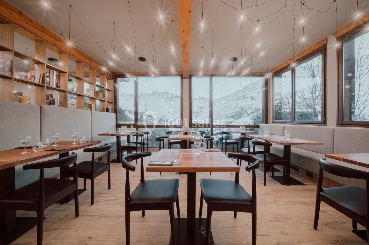 Salle de restaurant lumineuse avec grandes baies vitrées offrant une vue sur des montagnes enneigées.