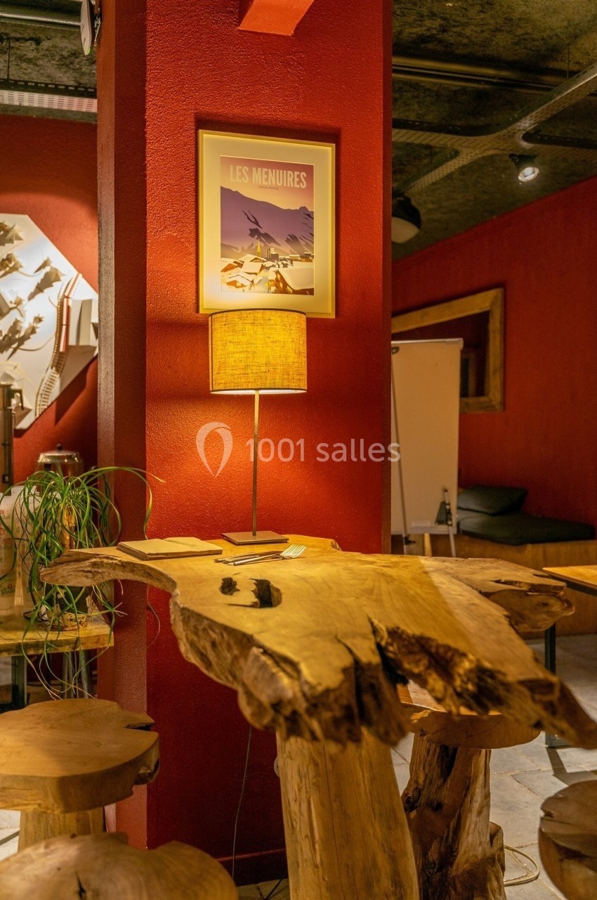 Table en bois brut avec tabourets assortis dans un intérieur chaleureux aux murs rouges, éclairé par une lampe.