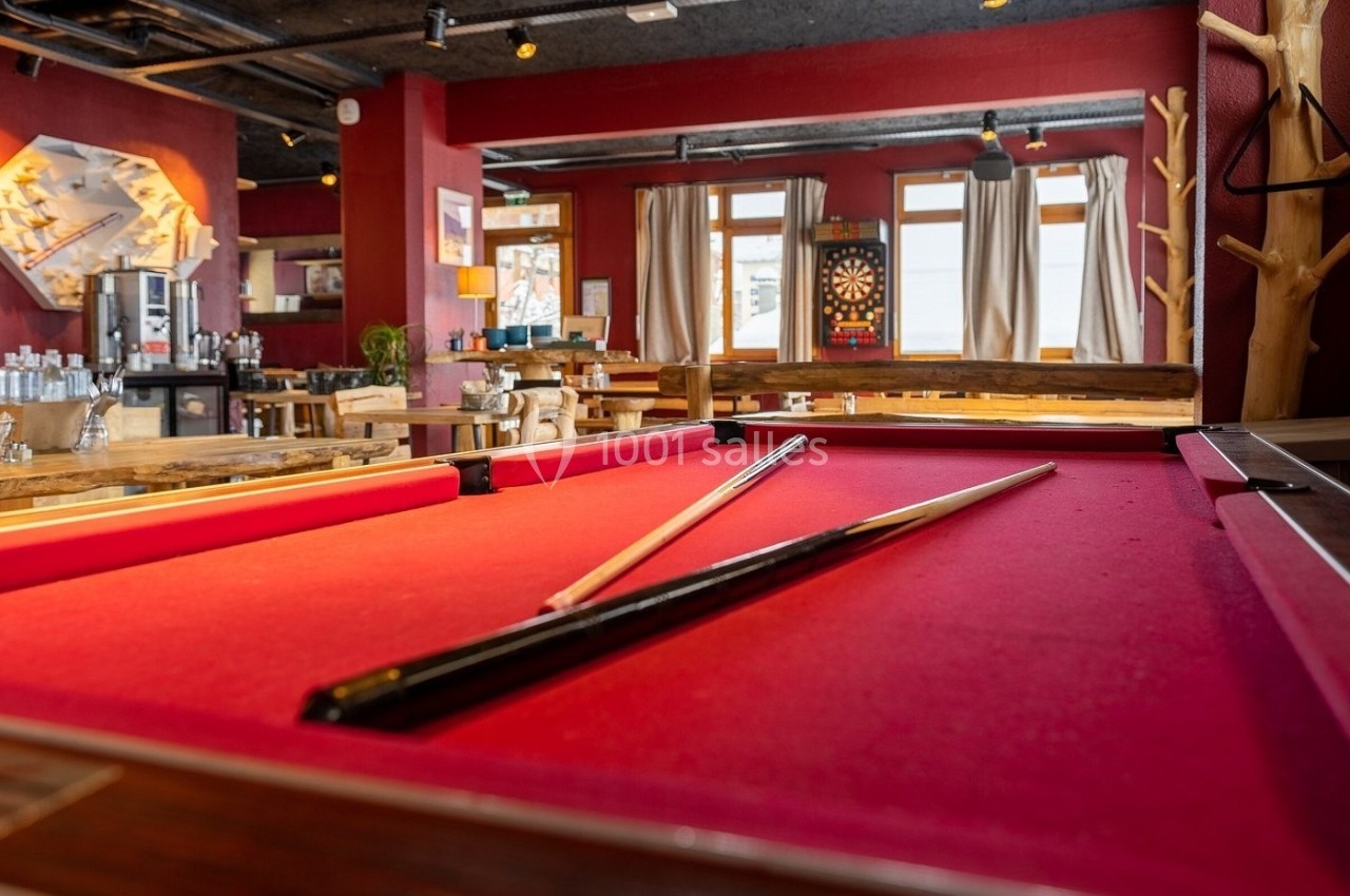 Table de billard rouge dans un bar chaleureux avec un jeu de fléchettes visible en arrière-plan.