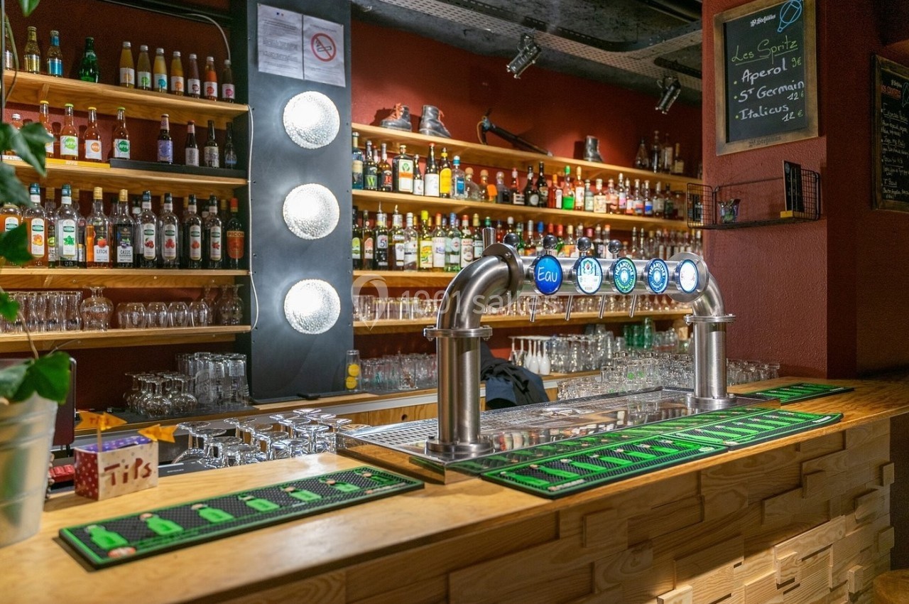 Comptoir de bar en bois avec tireuses à bière, étagères remplies de bouteilles et ambiance chaleureuse.