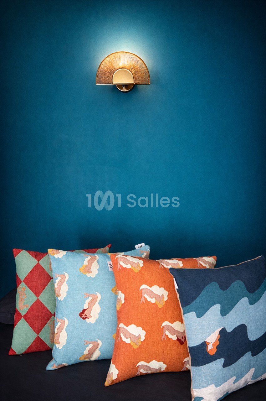 Applique murale en demi-cercle doré sur mur bleu pétrole, coussins colorés en premier plan.