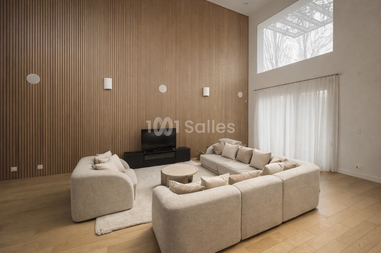 Salon spacieux avec canapés beige modulables, mur à lamelles bois, baies vitrées et éclairage zénithal.