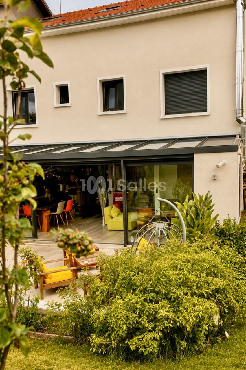 Terrasse couverte d'une maison avec baie vitrée, mobilier coloré et vue sur jardin paysagé.