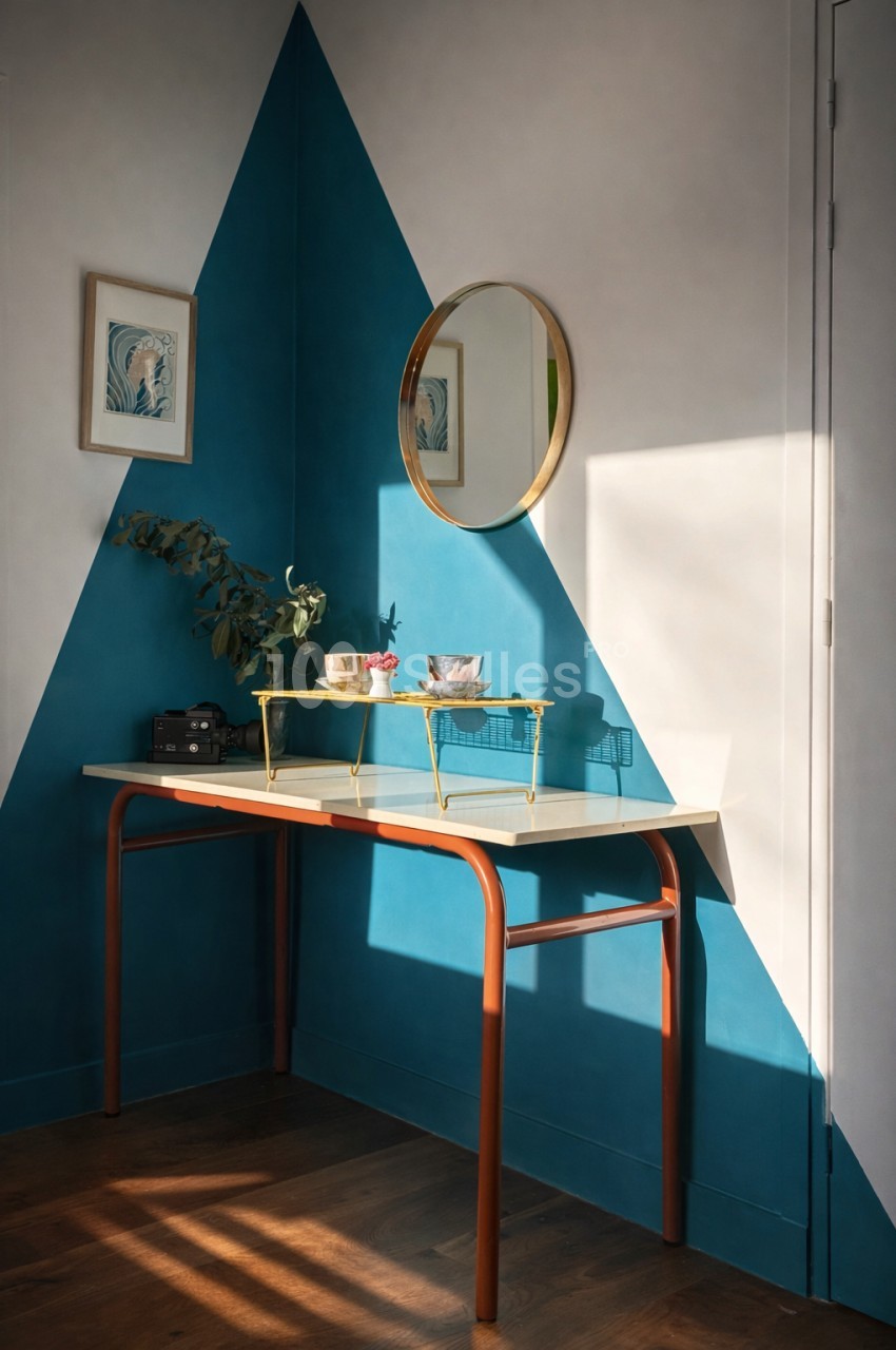 Alcôve peinte en bleu canard avec bureau blanc, chaise orange, miroir rond et gravures encadrées.