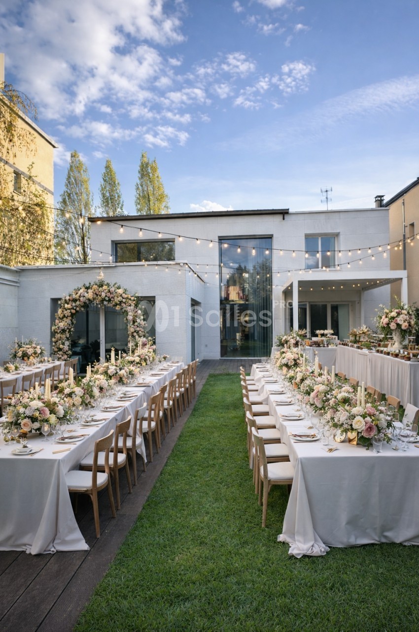 Cour intérieure dressée pour mariage avec tables longues, chaises en bois, fleurs blanches et guirlandes lumineuses.