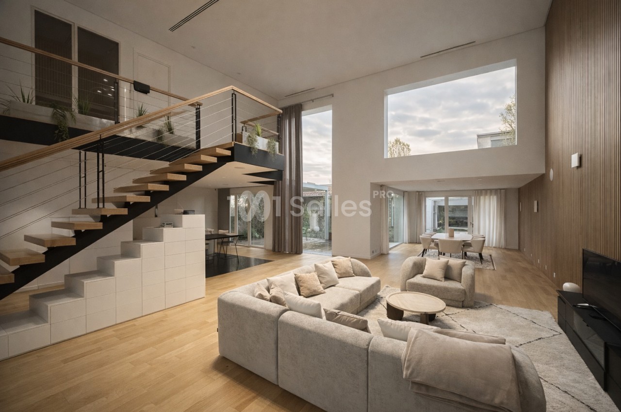 Intérieur spacieux avec salon au rez-de-chaussée, escalier en bois et mezzanine, baies vitrées donnant sur jardin.