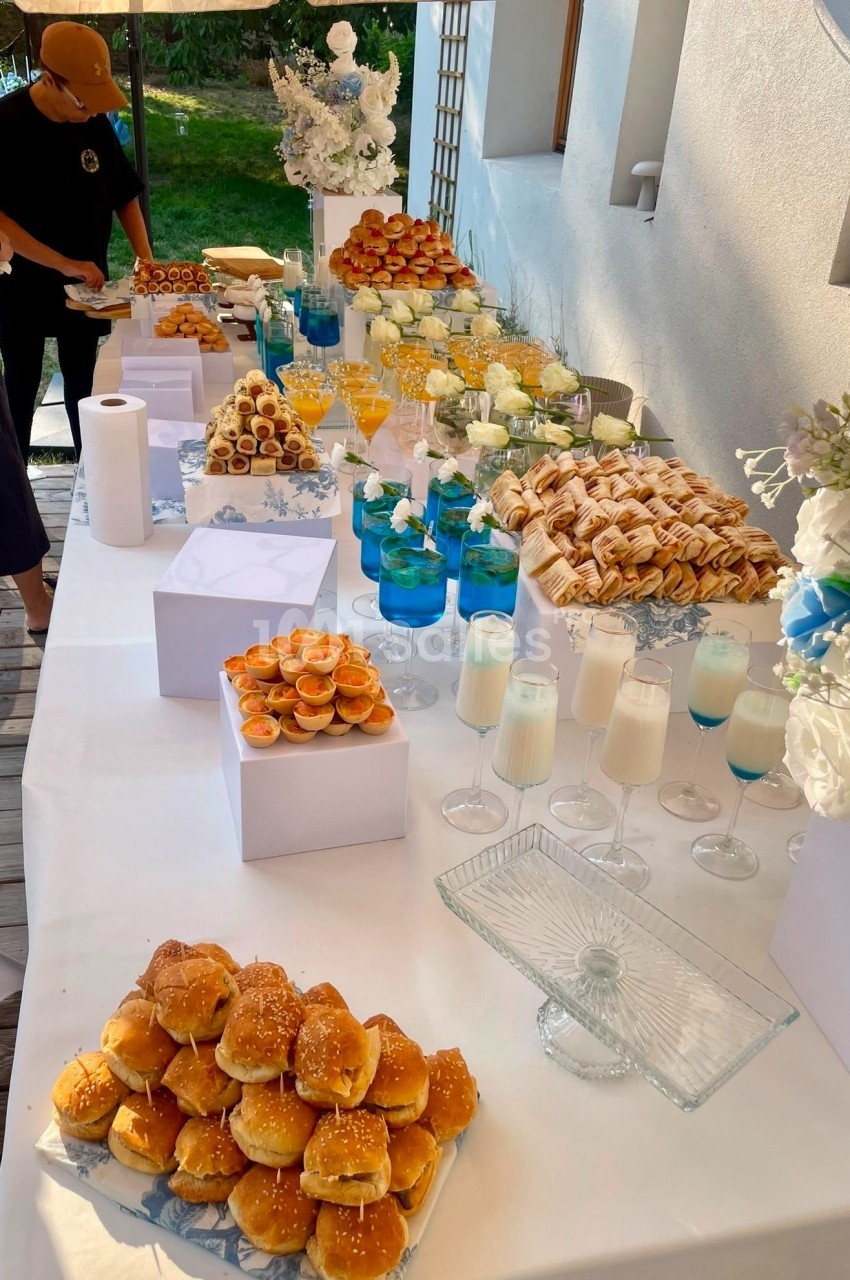 Table dressée en terrasse avec pains au sésame, viennoiseries, coupes de jus de fruits et bougies blanches.