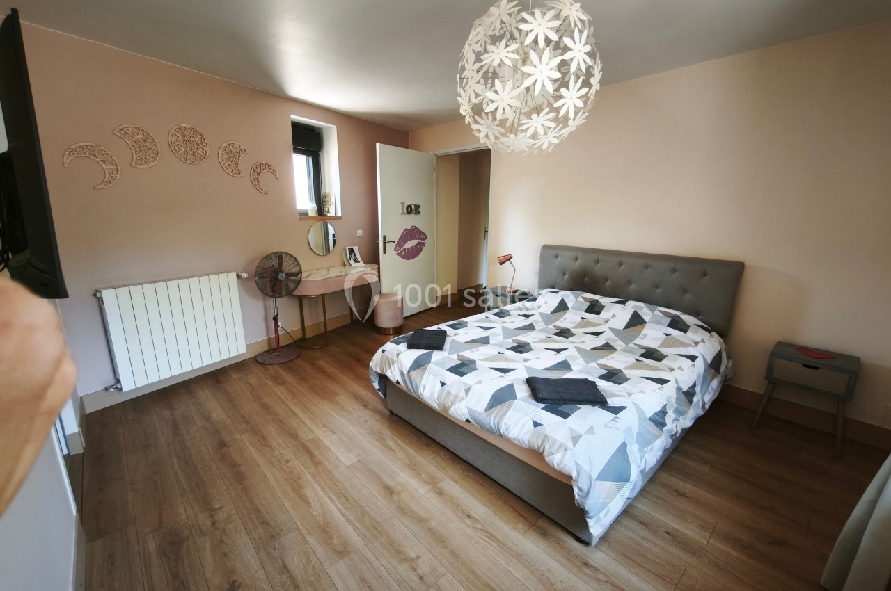 Chambre lumineuse avec lit double, parquet, bureau, décoration murale et suspension florale blanche.