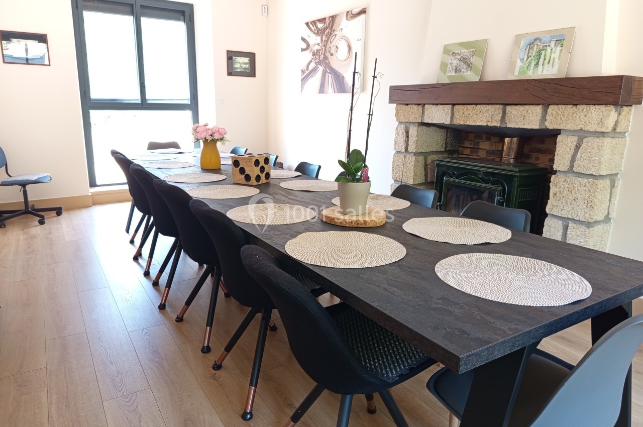 Grande table en bois sombre avec des sets de table ronds, entourée de chaises noires dans une salle lumineuse.