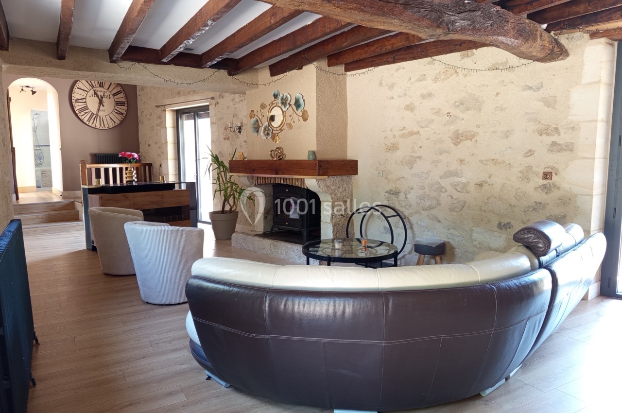 Salon avec poutres apparentes, murs en pierre, canapé en cuir, cheminée, et décoration murale.