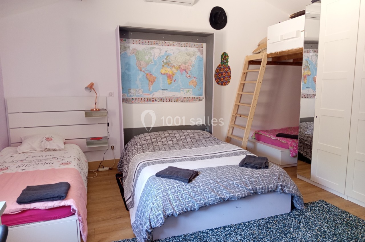 Chambre avec un lit double, un lit simple, un lit superposé, une carte du monde au mur et un tapis bleu au sol.