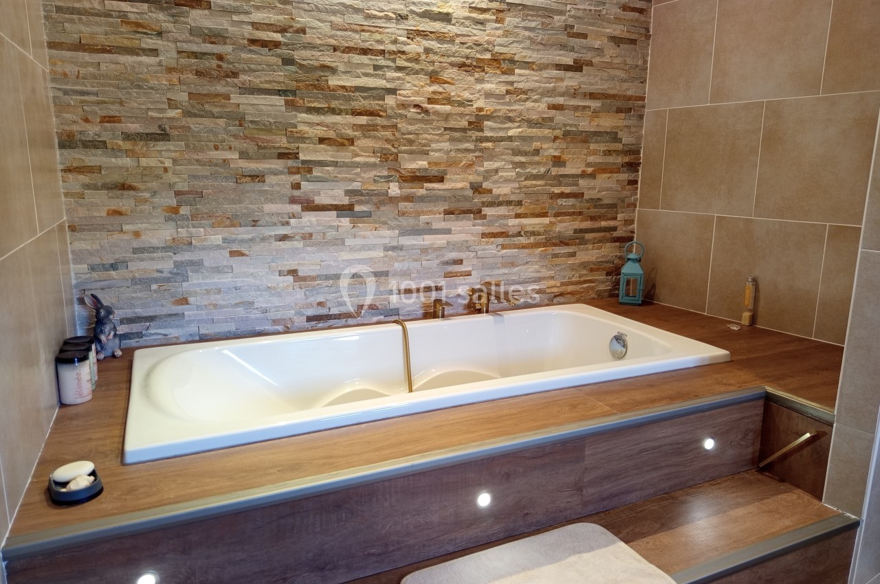 Baignoire encastrée avec revêtement en bois, mur en pierre apparente et éclairage intégré sur les marches.