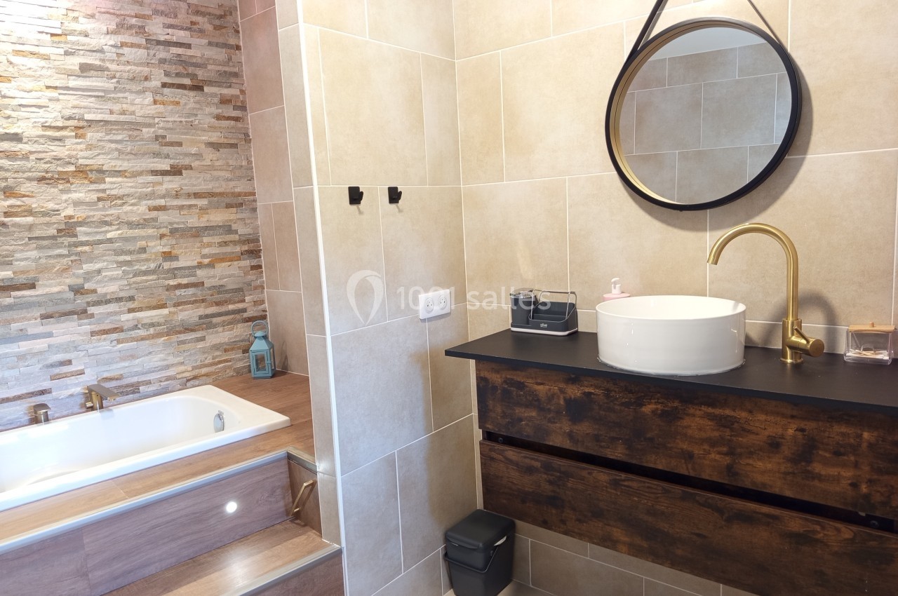Salle de bain moderne avec baignoire encastrée, vasque ronde sur meuble en bois et miroir rond suspendu.