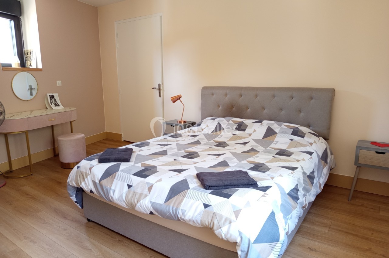 Chambre lumineuse avec un lit double, une parure géométrique, une coiffeuse et un sol en parquet clair.