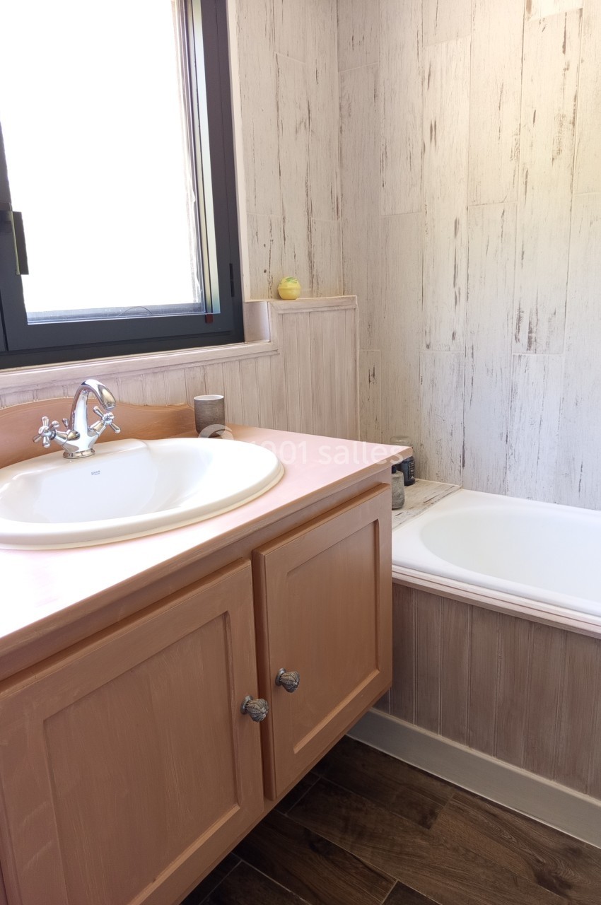 Salle de bain avec lavabo sur meuble en bois, baignoire blanche et mur à revêtement effet bois clair.