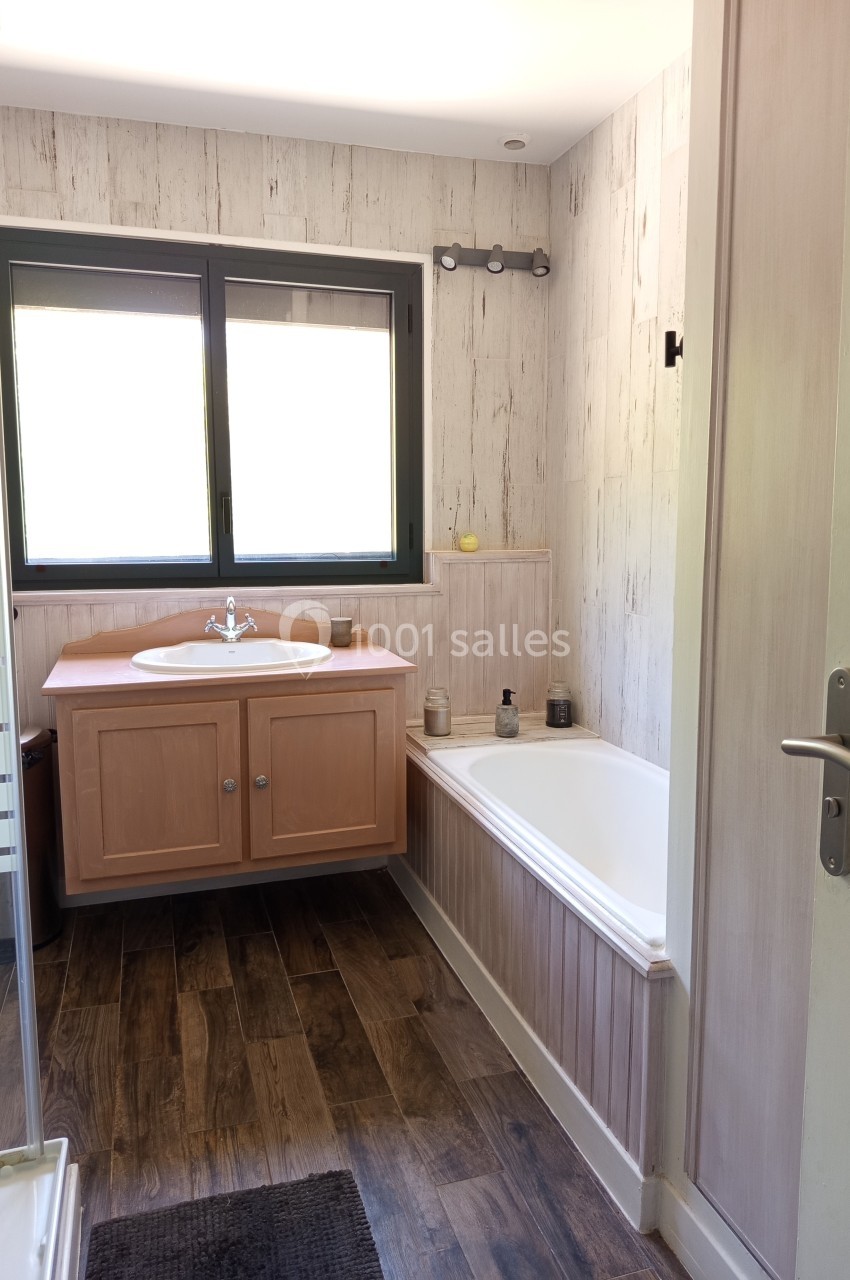 Salle de bain lumineuse avec baignoire, lavabo sur meuble en bois, fenêtre et sol en parquet foncé.