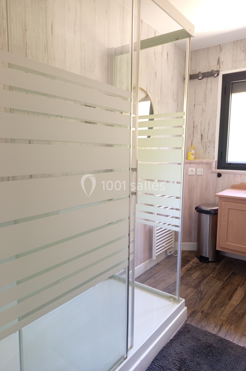 Douche avec parois vitrées à motifs, située dans une salle de bain lumineuse avec sol en bois et fenêtre.