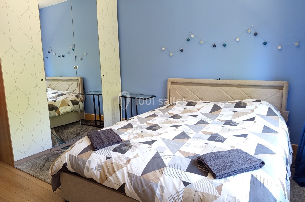 Chambre avec lit double, linge de lit géométrique, murs bleus, armoire à miroir et guirlande lumineuse décorative.