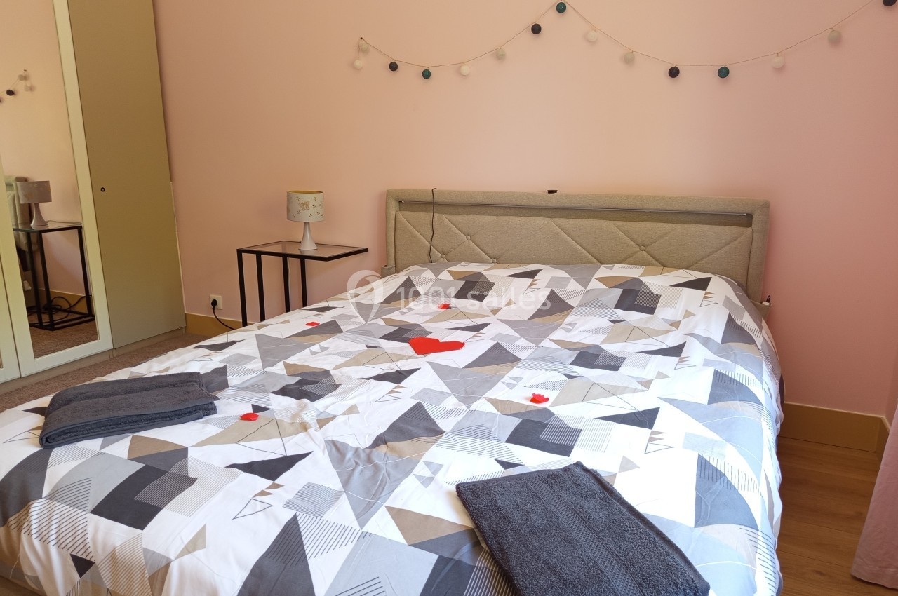 Lit double avec une housse de couette géométrique, deux serviettes pliées et une guirlande lumineuse au mur.