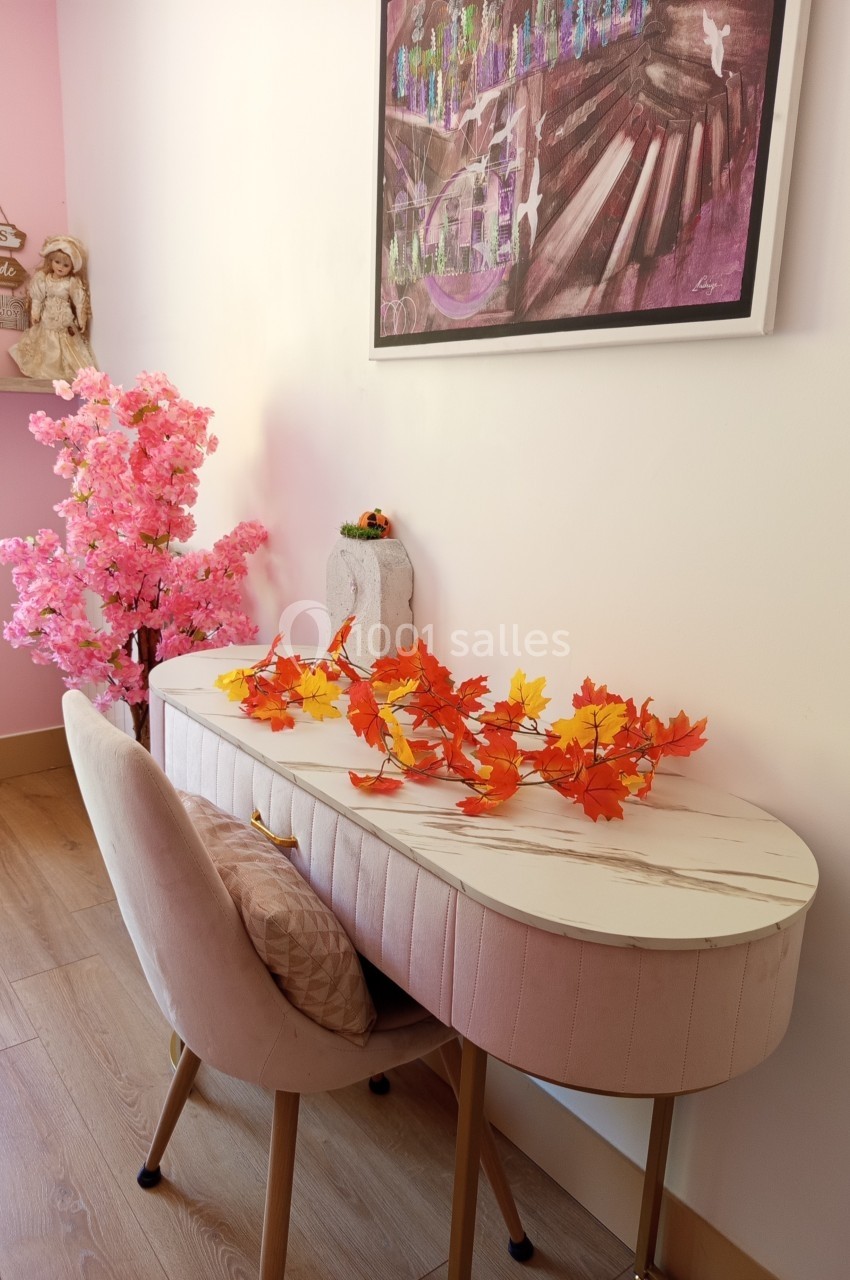 Bureau blanc avec chaise rose, décoré de feuilles d'automne et d'un tableau coloré sur un mur rose pâle.