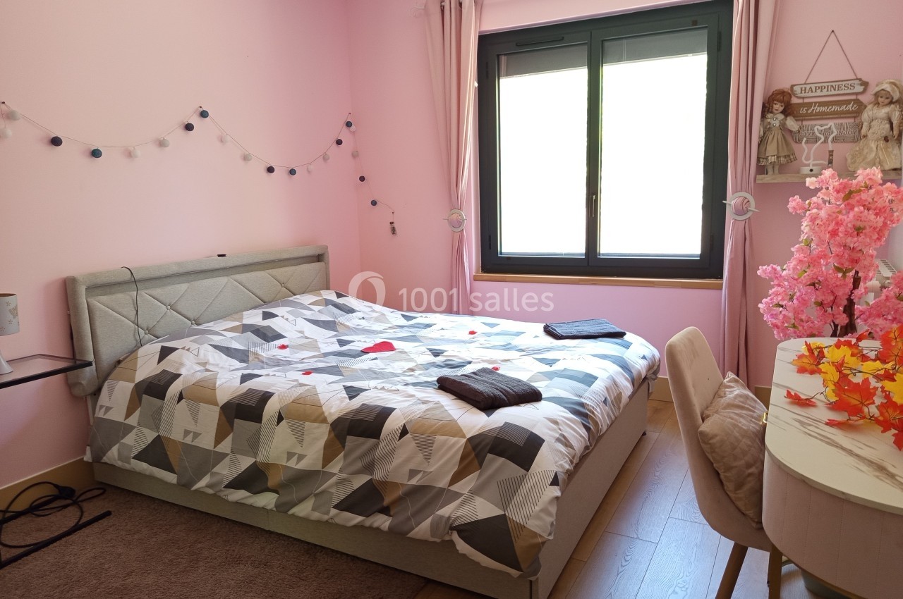 Chambre lumineuse avec murs roses, lit double à motifs géométriques, guirlande lumineuse et bureau décoré de fleurs.