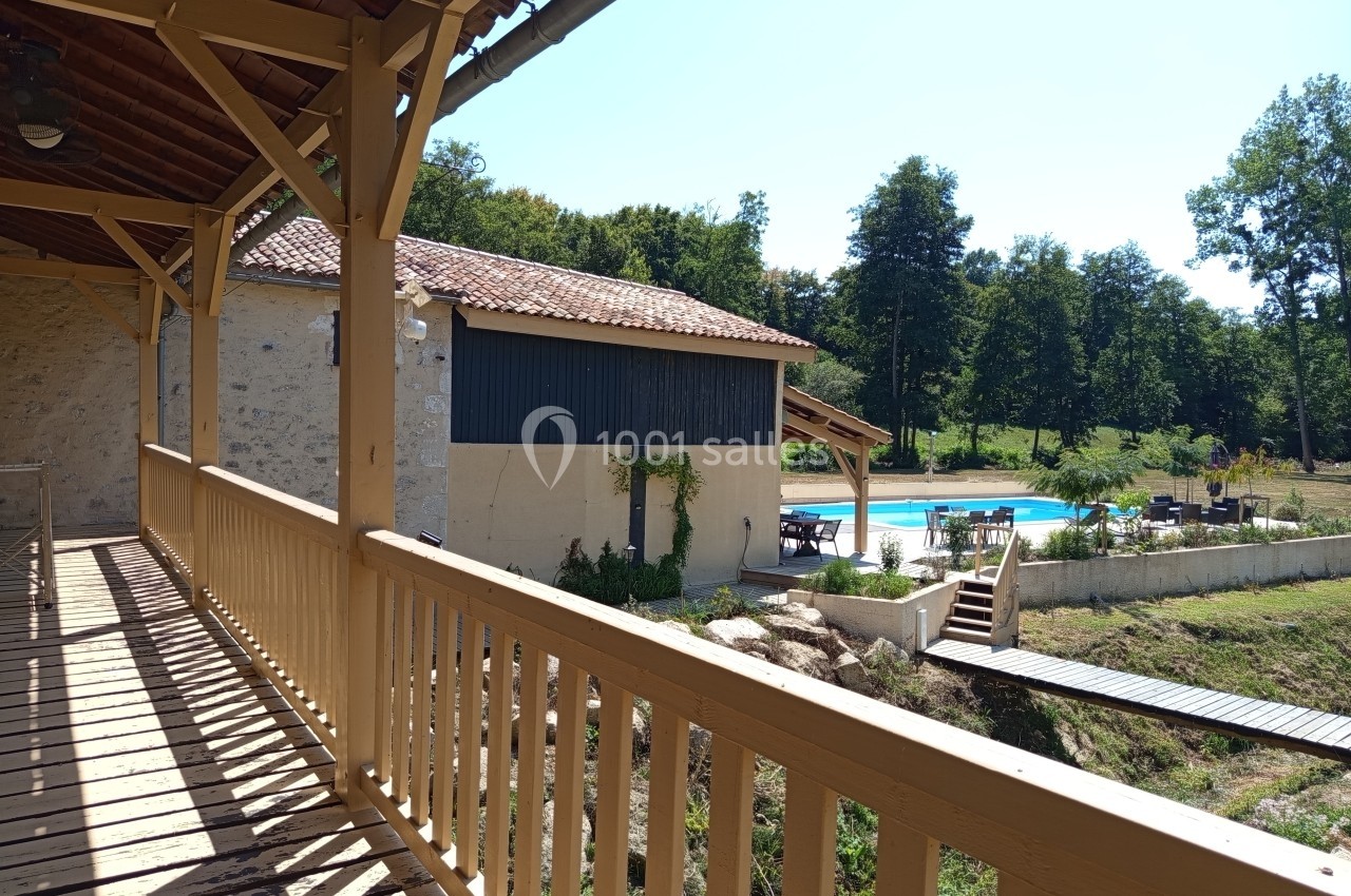 Vue depuis une terrasse en bois sur une piscine extérieure entourée de verdure et d'un bâtiment en pierre.