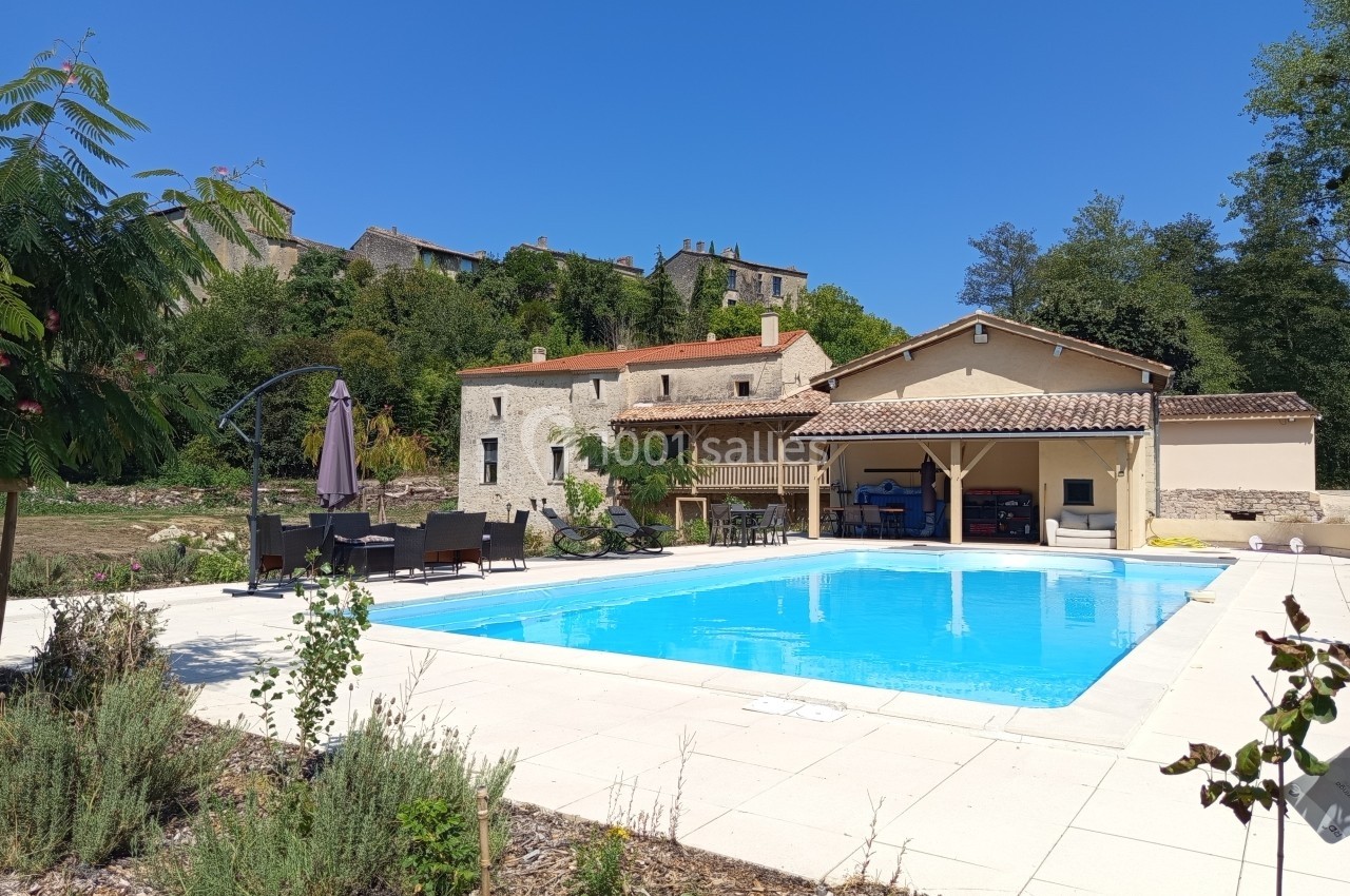 Maison en pierre avec piscine extérieure, terrasse aménagée et végétation environnante sous un ciel dégagé.