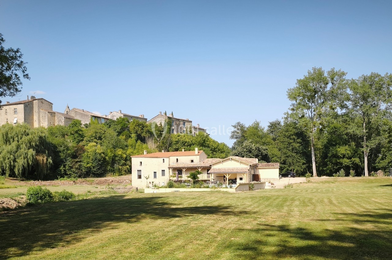 Maison en pierre avec jardin, située au pied d'un village perché entouré d'arbres et de verdure.