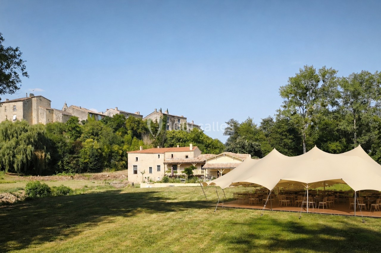 Tente beige installée sur une pelouse, près d'un bâtiment ancien entouré de verdure et d'arbres.