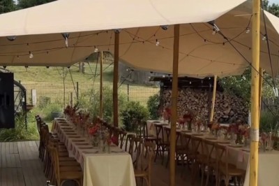 Tables décorées pour un dîner en plein air sous une tente éclairée de guirlandes lumineuses, près d'un bâtiment en pierre.
