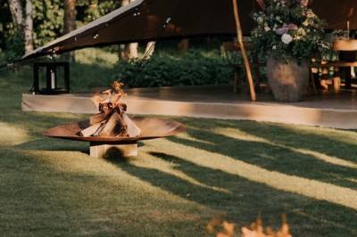 Tables décorées pour un dîner en plein air sous une tente éclairée de guirlandes lumineuses, près d'un bâtiment en pierre.