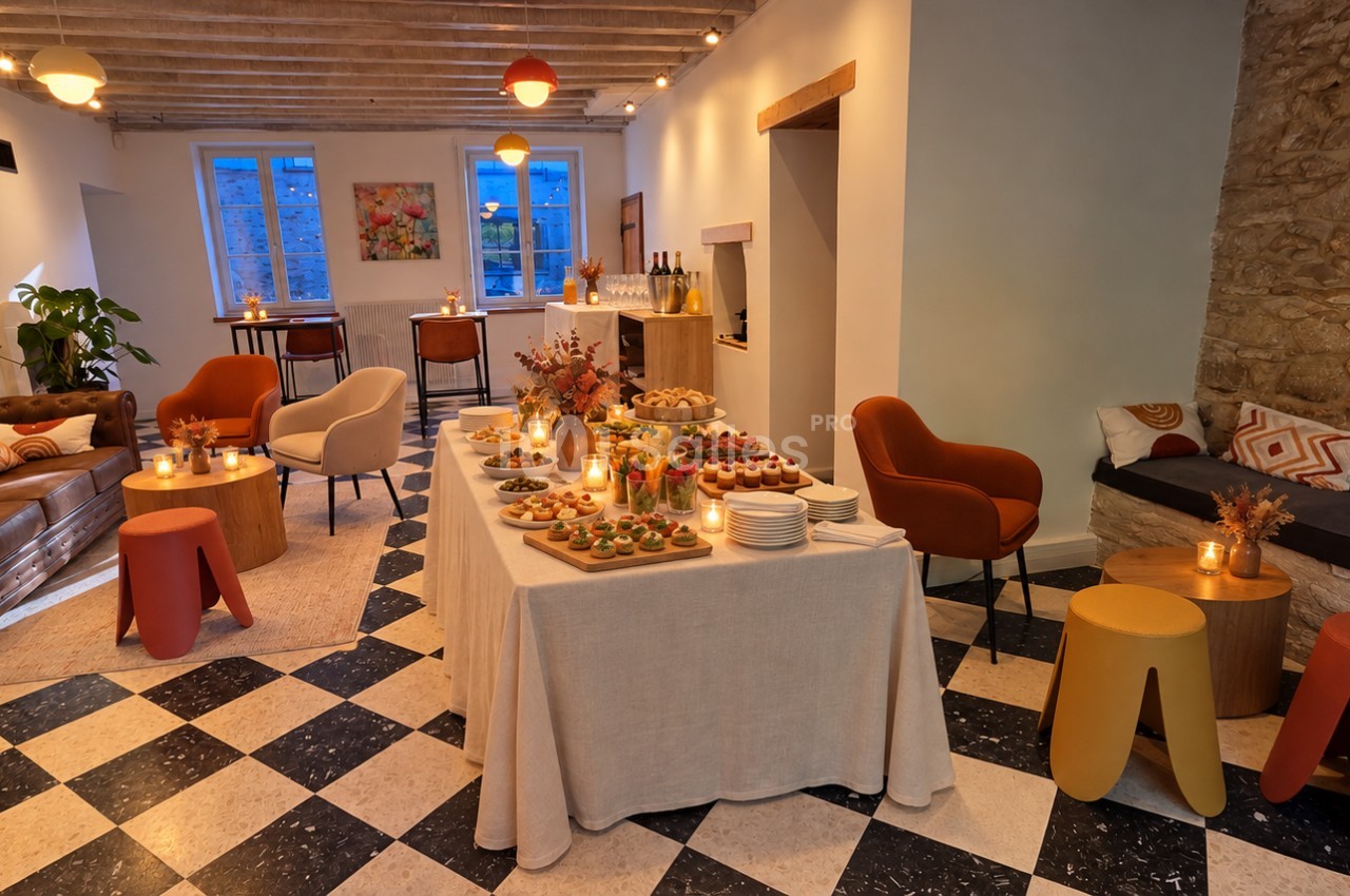Salle aux sol en damier noir et blanc avec un buffet dressé de petites bouchées sur nappe lin, entourée de fauteuils orange et de poufs colorés.